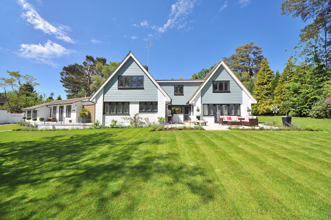 home-img Modern family home exterior showcasing a large lawn and garden under a clear blue sky.